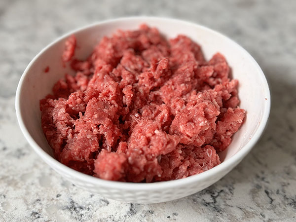 A bowl with ground beef mixed with salt and baking soda to tenderize.