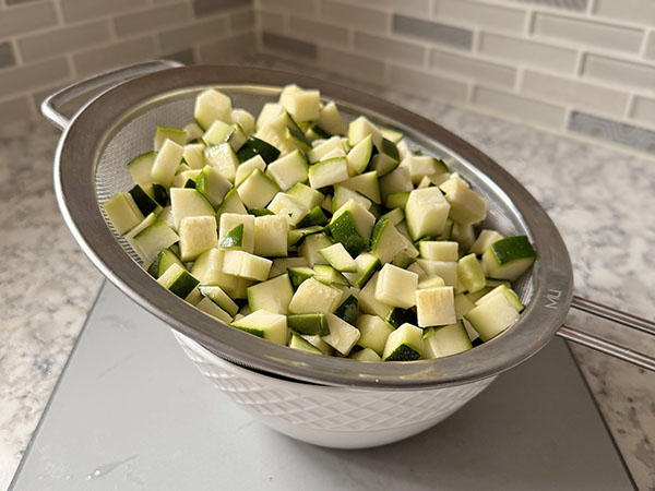 Colander filled with fresh zucchini cubes.