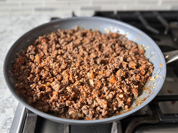 Browned ground beef in a skillet, mixed with marinara sauce and thyme.
