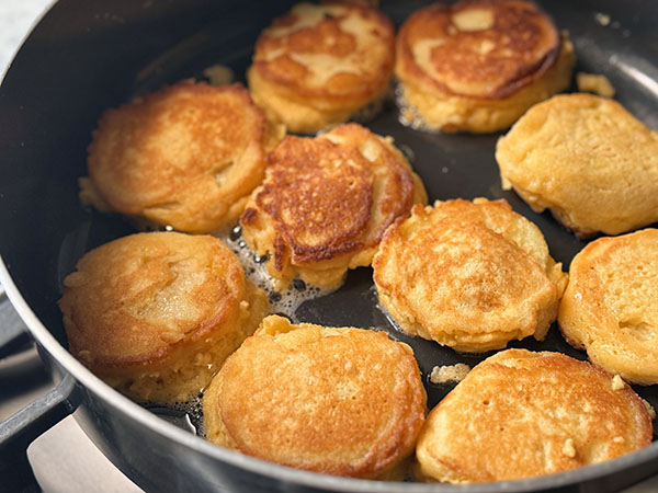 Flipped golden brown apple donut pancakes in a skillet.