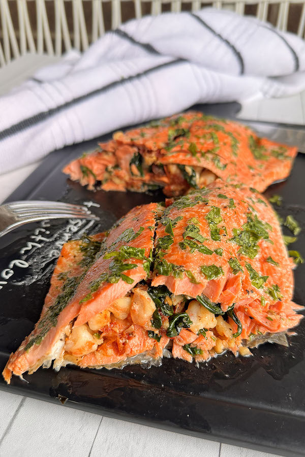 Baked salmon stuffed with Tuscan style shrimp on a serving board, cut in two portions, to showcase the filling.