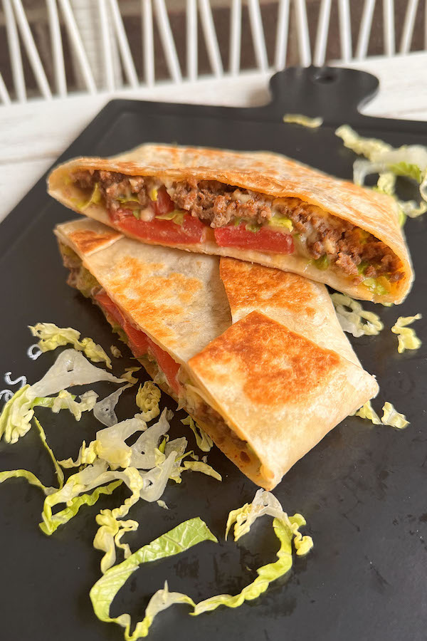 Ground Beef Tortilla Wrap cut in half with the delicious taco meat, veggies and cheese filling exposed.