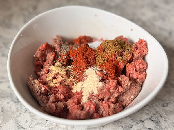 Raw ground beef in a bowl with homemade taco seasoning ingredients on top.