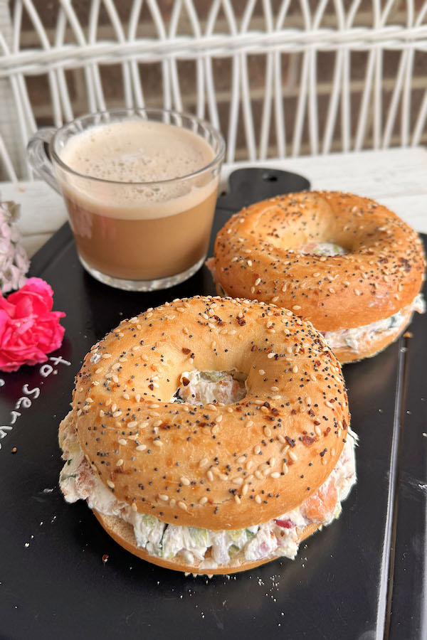 Breakfast Bagel Sandwiches with Salmon and Cream Cheese on a serving board with a cup of coffee and flowers next to them.