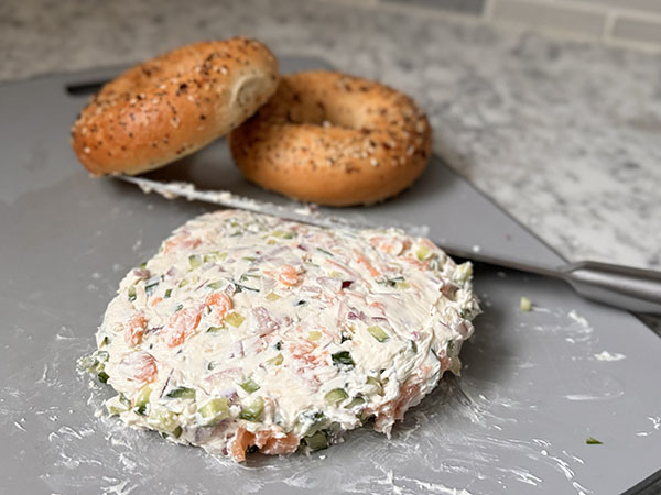 Combined salmon, onion, cucumber and cream cheese spread for bagel breakfast sandwich on a cutting board.