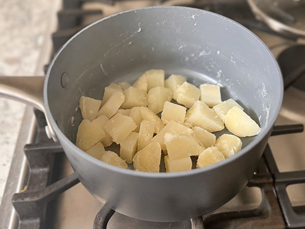 Parboiled potato cubes drained in a pot.