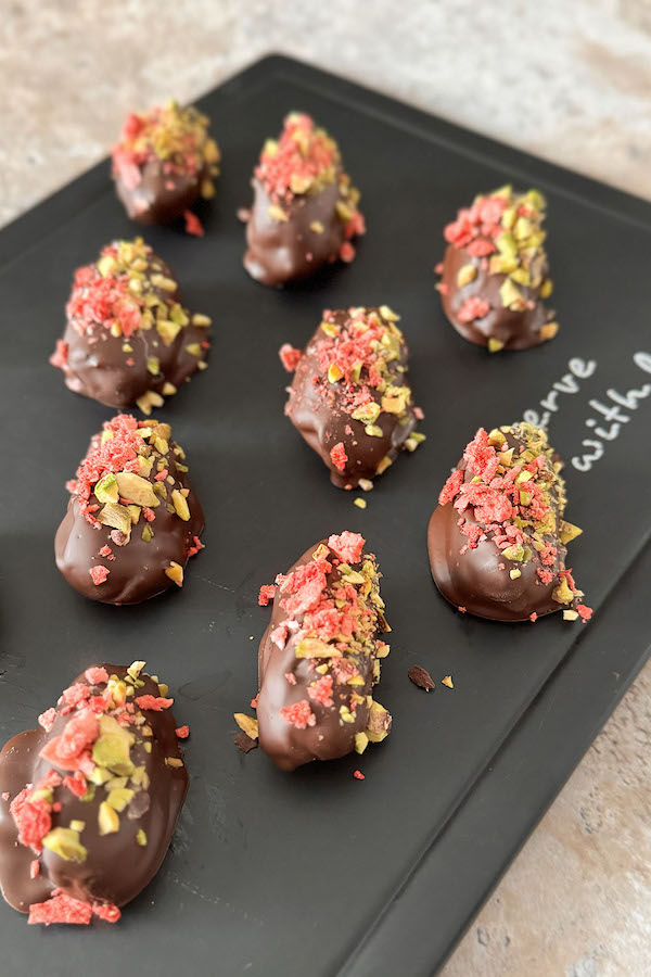 Chocolate dates with almond butter, pistachios and strawberries on a serving board.