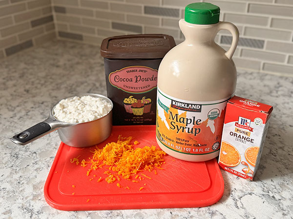 Ингредиенты для шоколадно-апельсинового мусса: зернистый творог, кленовый сироп, како-порошок, апельсиновый экстракт и апельсиновая цедра.