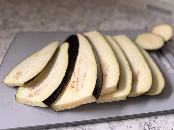 Eggplant sliced lengthwise on a cutting board.