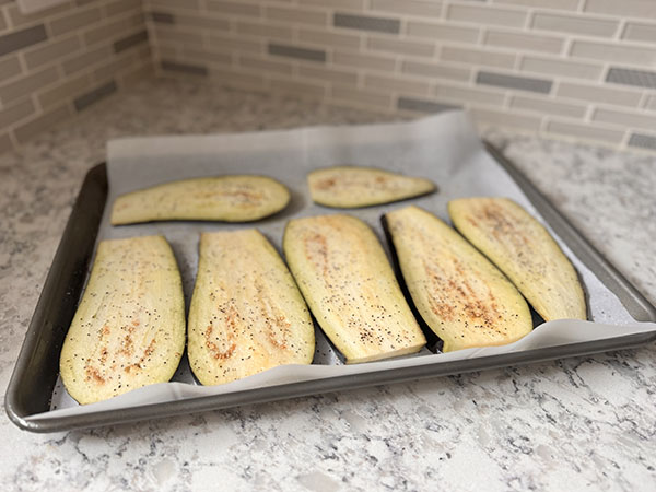 Eggplant slices on a baking sheet seasoned with salt and pepper.
