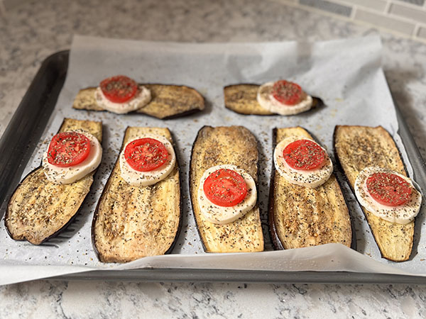 Baked eggplant slices topped with mozzarella and tomato, seasoned with basil and oregano.