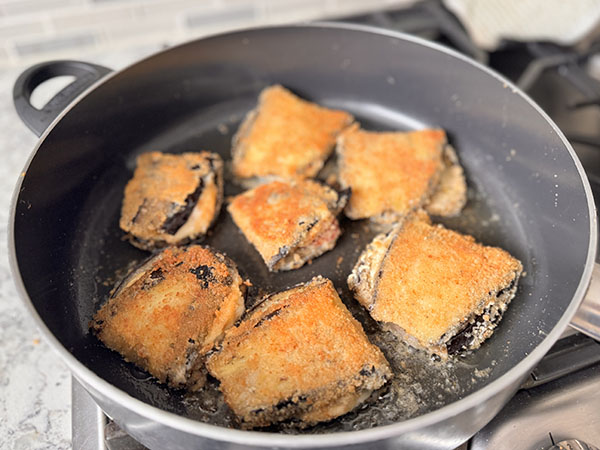 Breaded eggplant pockets browning in a skillet.