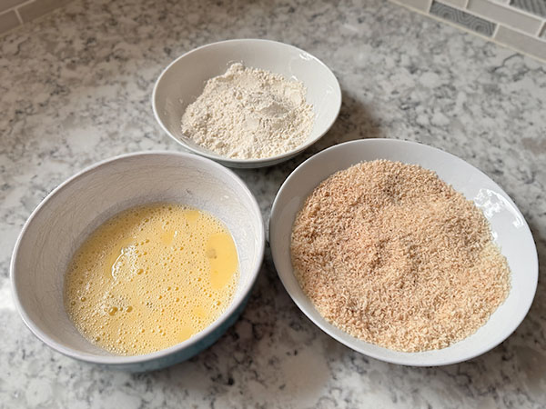 Breading station with flour plate, egg mixture plate and panko breadcrumbs with seasonings plate.