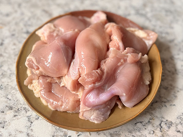 Raw chicken thighs seasoned with salt in a bowl.