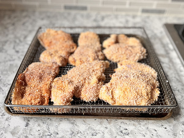 Panko coated chicken thighs in an air fryer basket.