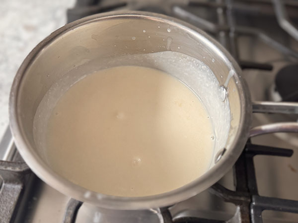 Sweet creamy coconut sauce in a saucepan on stove top.