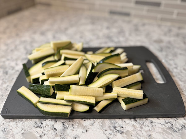 Zucchini sliced into sticks sitting on a cutting board.