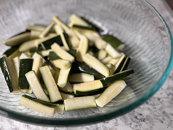 Zucchini sticks in a bowl coated with oil.