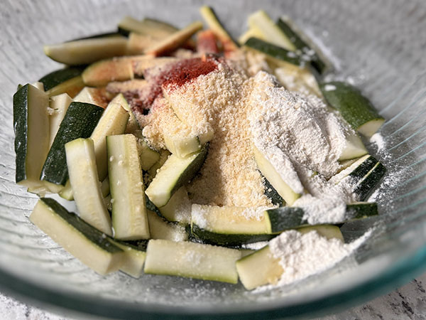 Zucchini sticks in a bowl with seasonings on top.