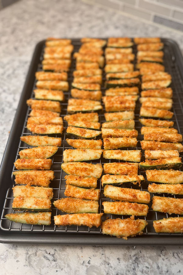 Zucchini sticks coated with flour and seasonings, arranged on a baking rack.