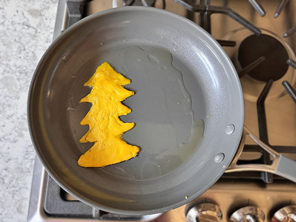 Елочка, нарисованная яичными желтками готовится на сковороде.