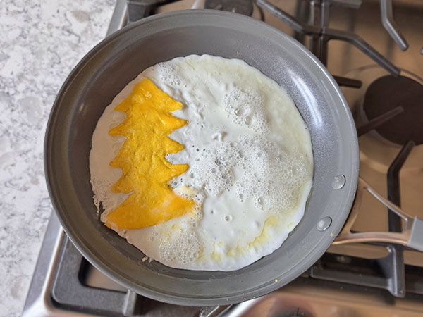 Egg whites added around the egg yolks Christmas tree cooking in a skillet.