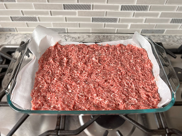 Meat mixture spread in a glass dish, prepared for the sausages.