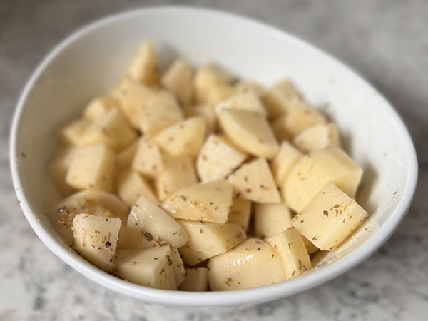  Картофель, перемешанный со специями в миске.