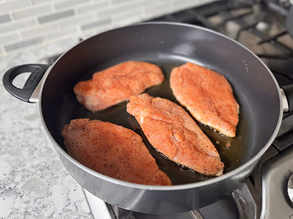 Chicken breasts frying in a skillet.