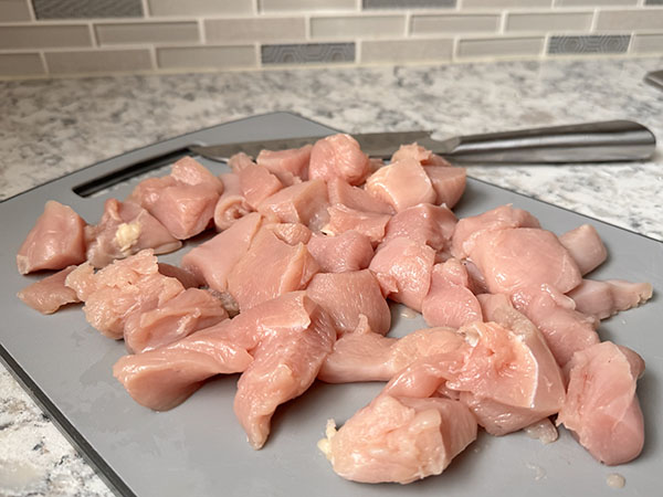 Raw chicken breasts cut into bite-sized pieces on a cutting board.