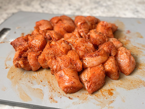 Chicken breast pieces coated in spices on a cutting board.