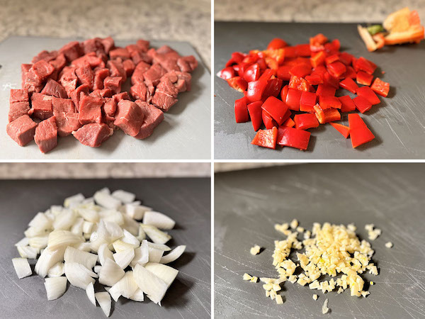 Prepared curry ingredients: beef cut into cubes, chopped red bell pepper, chopped onion and minced garlic on cutting boards.