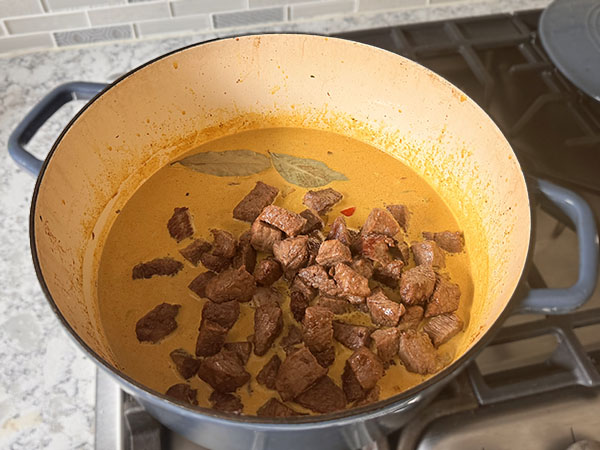 Beef added to coconut curry sauce for cooking.