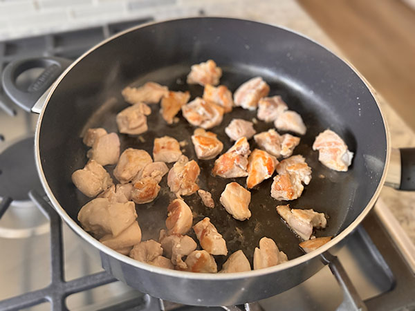 Золотисто-коричневые кусочки курицы жарятся в сковороде.