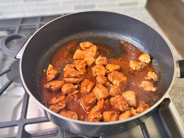 Курица жарится в сковороде в корейском соусе до его загустения.