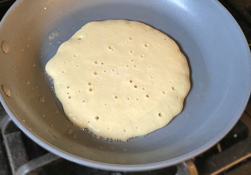 Cooking a large pancake on a skillet until bubbly.
