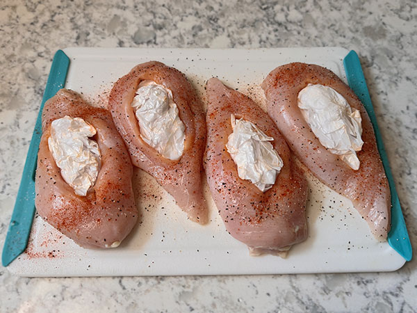 Raw seasoned chicken breasts with crumpled parchment paper inside their pockets to help them keep shape.