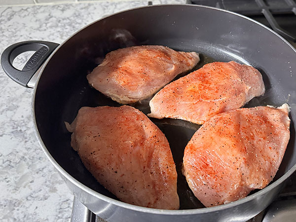 Chicken breasts in a large pan in the process of searing.