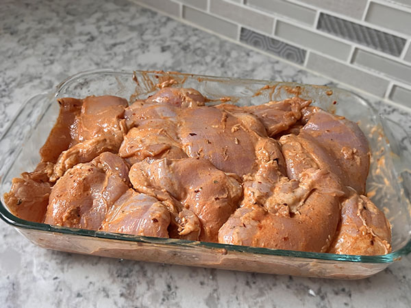 Shawarma marinade coated chicken thighs in a glass dish.