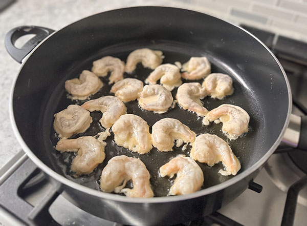 Shrimp dipped in tempura batter frying in a skillet.