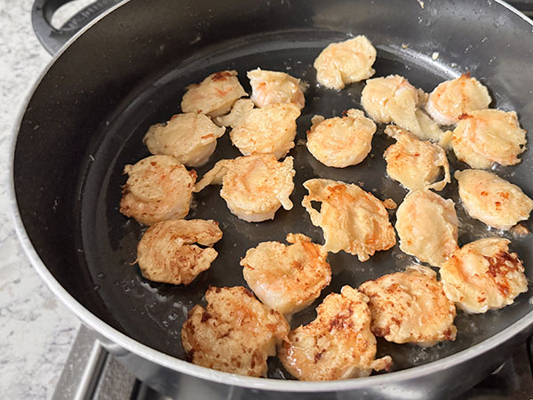 Pink and slightly golden brown shrimp frying in a skillet.