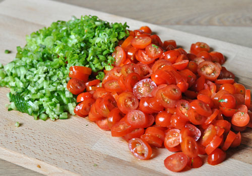 Chopped fresh tomatoes, cucumber and green onions on a cutting board.