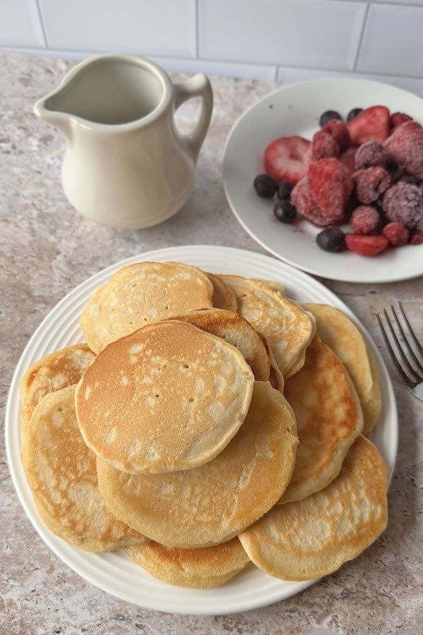 Pile of pancakes made without milk on a plate served with berries on the side.