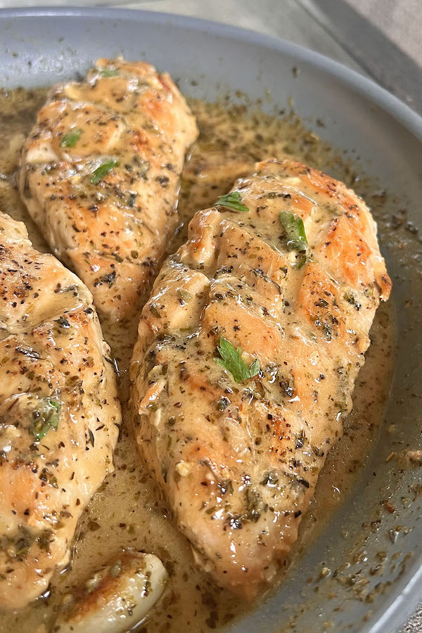 Juicy chicken breasts in a pan with lemon mustard sauce, topped with fresh parsley.