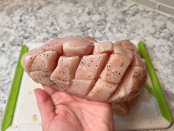 Raw boneless skinless chicken breast scored in a crosshatch pattern for better cooking.