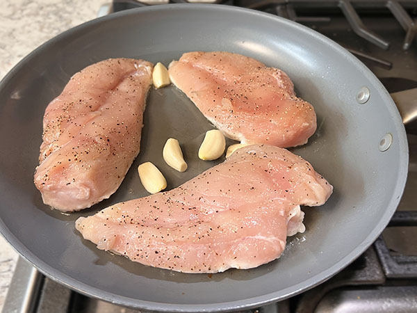 Chicken breasts searing in a skillet along with garlic cloves.