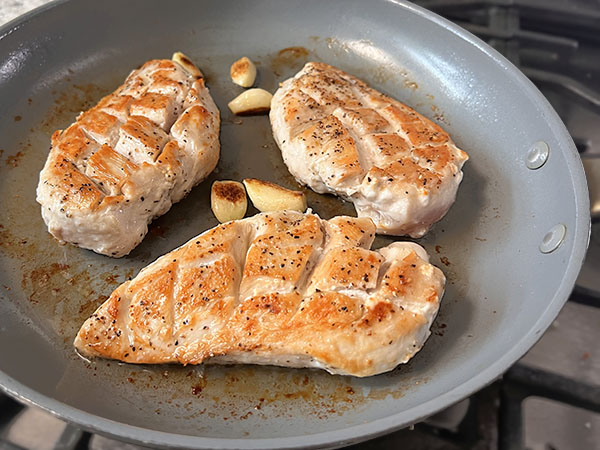 Flipped pan-seared golden brown chicken breasts in a skillet.