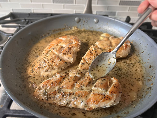 Golden brown chicken breasts  in a skillet with lemon-mustard sauce spooned over.