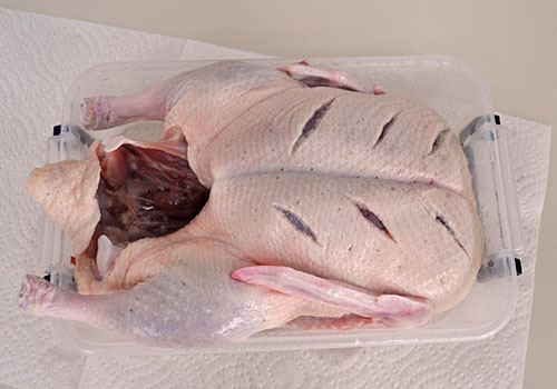 Whole duck with a few skin cuts, prepared for roasting in the oven.