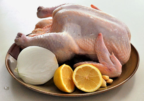 Целая сырая тушка курицы с ингредиентами для запекания: лимоном, луком и чесноком.